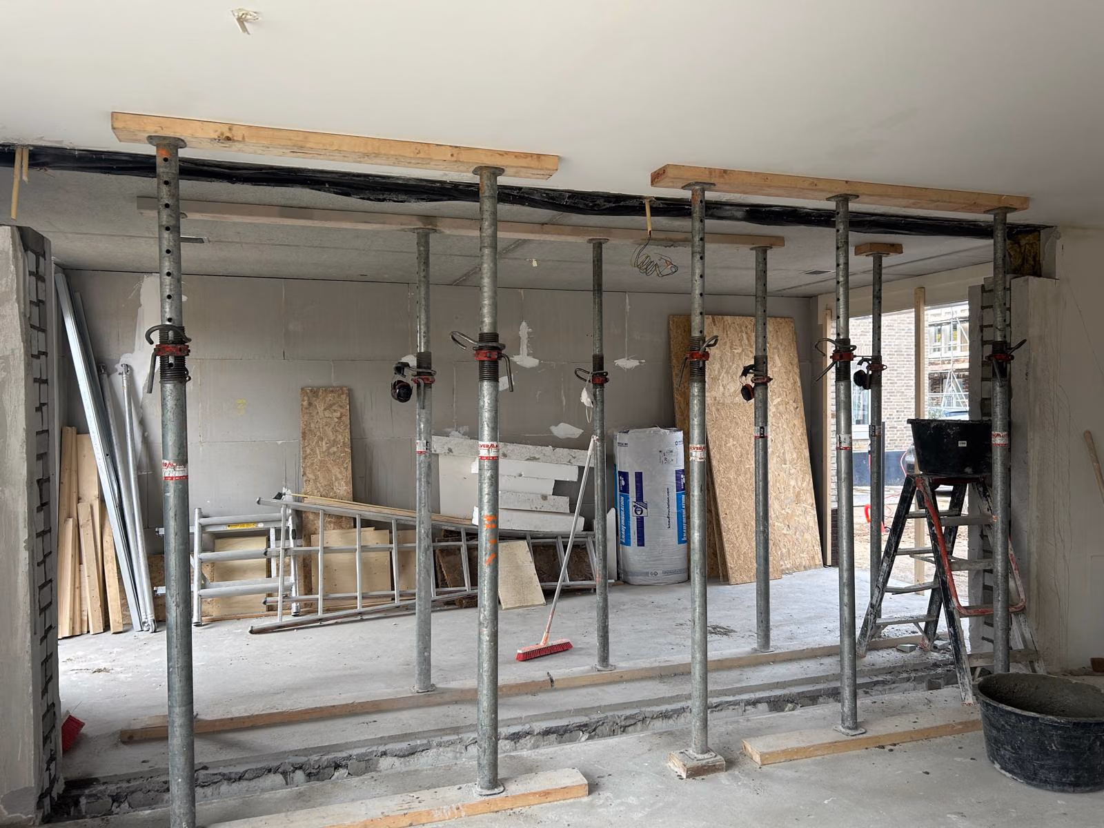 Muurdoorbraak met stalen stempels en houten balken die het plafond tijdelijk ondersteunen boven de nieuwe opening