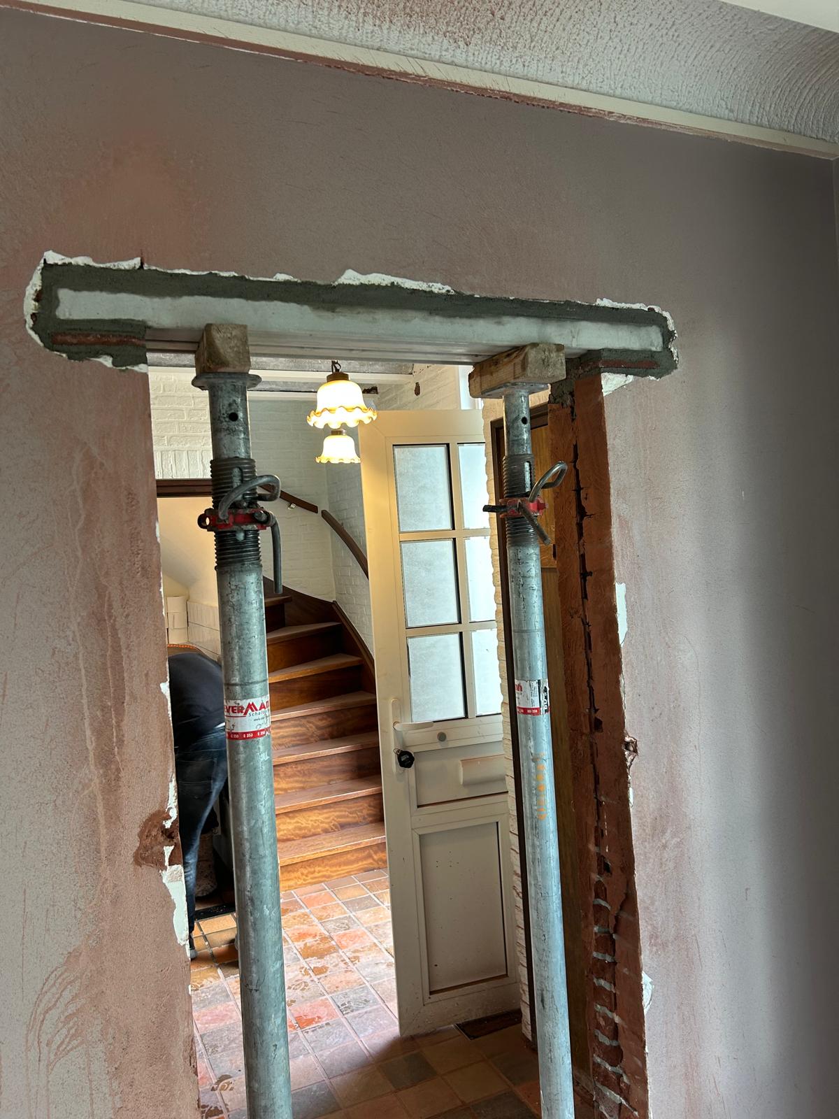 Muurdoorbraak met rode stalen balk en stempels bij het sparing maken in muur van een woning